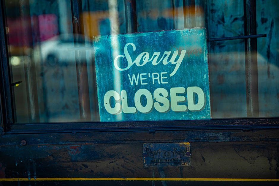 A rectangular illuminated sign mounted on a dark wall displays the message 'SORRY WE'RE CLOSED' in bold black capital letters. The sign has a black frame surrounding a light orange or beige background