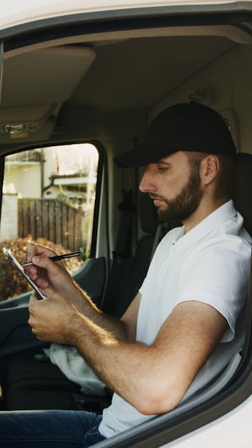 The image shows the open rear of a white van parked outdoors, likely on a residential street, with a large interior filled with stacked cardboard boxes of various sizes. Two movers, a man and a woman,